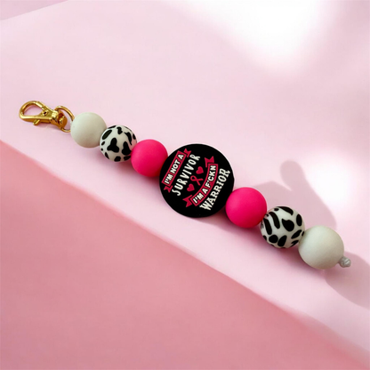 Keychain with colorful beads and a 'Survivor' button on a pink background