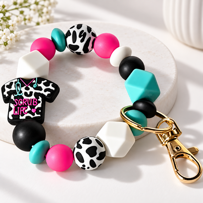 Scrub Life cow print nurse beaded wristlet keychain with hot pink, teal, black and white silicone beads and gold lobster claw clasp
