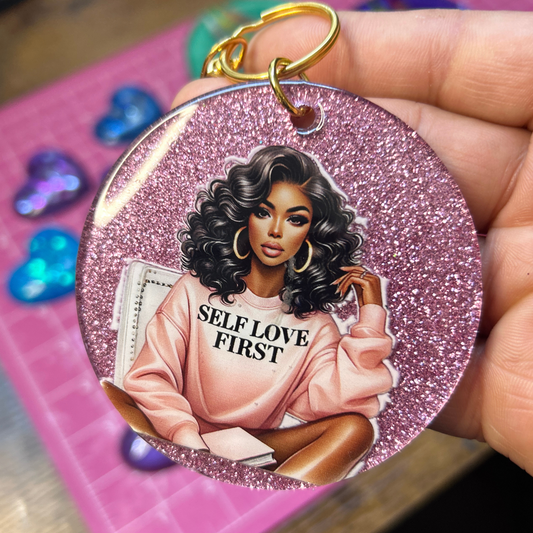 Pink glitter handmade resin keychain featuring “Self Love First” artwork and gold keyring attachment.